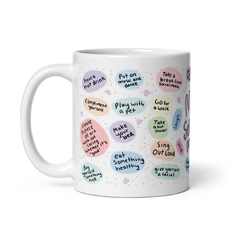 Peut inclure: Une tasse en c&eacute;ramique blanche avec un motif color&eacute; comportant des phrases comme "prendre une boisson chaude", "se complimenter", "jouer avec un animal de compagnie", "faire son lit", "manger quelque chose de sain", "faire une pause des m&eacute;dias sociaux", "aller se promener", "prendre une douche chaude", "chanter &agrave; tue-t&ecirc;te", "se faire un soin du visage", "rire" et "sourire".