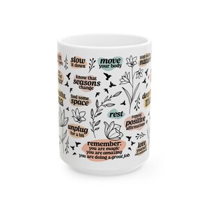May include: White ceramic mug with black text and floral illustrations. The mug features phrases like "slow it down," "move your body," and "remember: you are magic." The design includes birds and botanical elements.