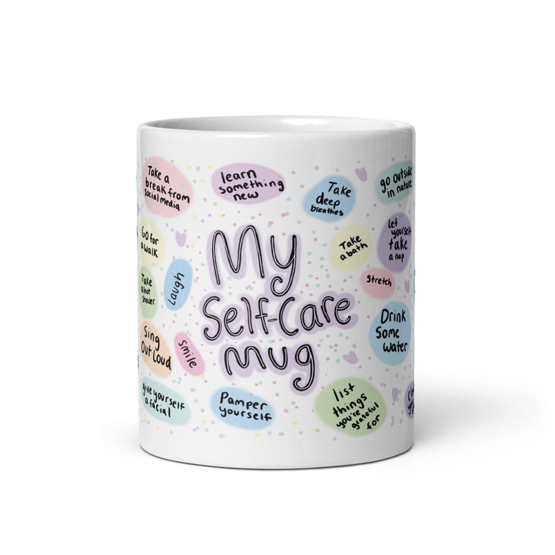Peut inclure: Une tasse en c&eacute;ramique blanche avec un motif rose, violet et vert. La tasse porte l'inscription "My Self-Care Mug". La tasse est entour&eacute;e de divers conseils de bien-&ecirc;tre, tels que "Prendre une pause des m&eacute;dias sociaux", "Faire une promenade", "Prendre un bain", "S'&eacute;tirer", "Boire de l'eau", "Lister les choses pour lesquelles vous &ecirc;tes reconnaissant", "Prendre soin de soi", et "Sourire".