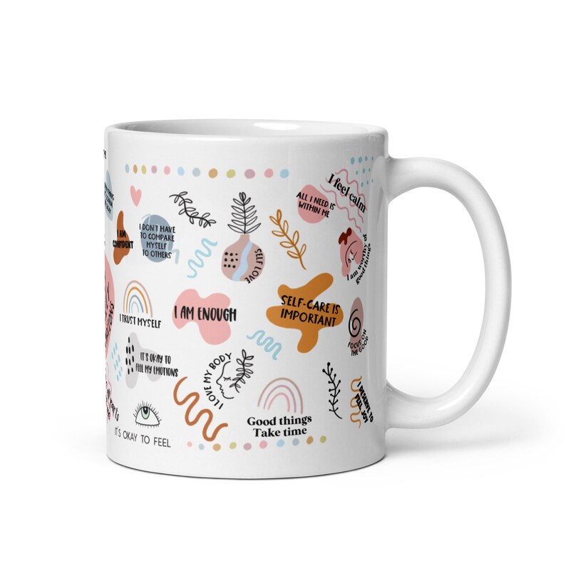 May include: White ceramic mug with a colorful design featuring positive affirmations and illustrations. The text includes phrases like "I am enough", "Self-care is important", "Good things take time", and "I trust myself".