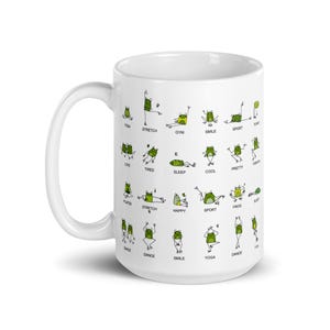 May include: White ceramic mug featuring green cartoon frogs in various yoga poses, with words like "stretch", "smile", and "yoga". The mug has a large handle and is suitable for hot or cold beverages.