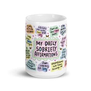 May include: White ceramic mug with colourful text and illustrations. The text reads "My Daily Sobriety Affirmations" and includes phrases like "I am worthy of joy" and "Life fills me with love and joy".
