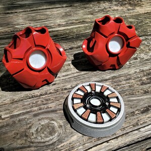 A pair of red robotic fingerless gloves and an electronic chest piece based on pieces of a superhero's suit provide examples of custom 3D printed cosplay pieces produced by the shop Nautolith Crafts.
