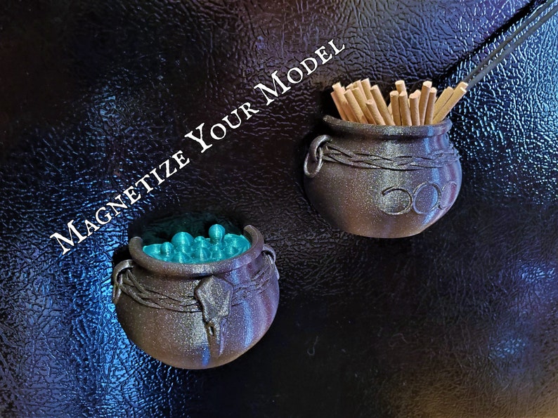 A pair of witch cauldron magnets on a refrigerator door with the nearby text "Magnetize Your Model" indicate that commissioned custom 3D printing projects can include hardware such as magnets.