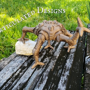 A bronze 3D printed version of a unique alien character from a popular book is posed outdoors partially standing on a rock to provide an example of an articulated posable custom 3D modeled and 3D printed design.