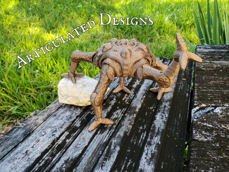A bronze 3D printed version of a unique alien character from a popular book is posed outdoors partially standing on a rock to provide an example of an articulated posable custom 3D modeled and 3D printed design.