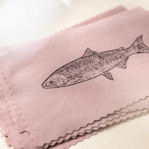 May include: A stack of pink fabric cloths with a black illustration of a fish. The fish is a side profile with detailed scales and fins. The cloths have a decorative, scalloped edge.