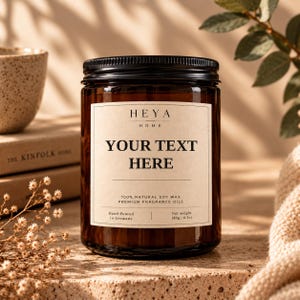 Peut inclure: Un pot de bougie en verre brun avec un couvercle noir et une étiquette beige. L'étiquette porte le texte HEYA HOME, YOUR TEXT HERE, 100% NATURAL SOY WAX, PREMIUM FRAGRANCE OILS, Hand-Poured in Germany, et net weight 180g / 6.3oz en noir.