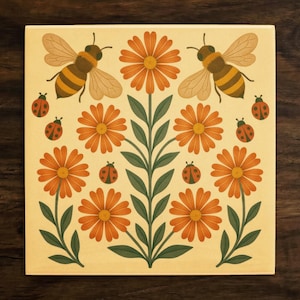 May include: Square tile with a floral design featuring orange daisies, green leaves, ladybugs, and bees. The tile has a cream-colored background and is set against a dark wood surface.