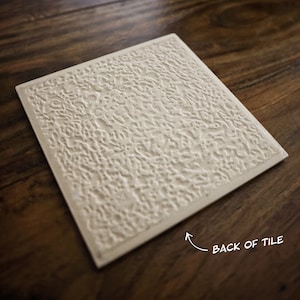 May include: The back of a white ceramic tile with a textured surface. The tile is on a wooden surface.