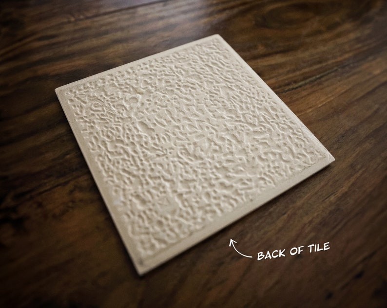 May include: The back of a white ceramic tile with a textured surface. The tile is on a wooden surface.
