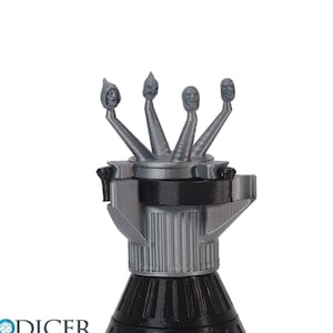 Könnte beinhalten: Ein silberfarbenes Raketenmodell mit fünf Köpfen oben. Die Köpfe sind alle nach vorne gerichtet und haben eine Kapuzenform. Die Rakete steht auf einem schwarzen Sockel.