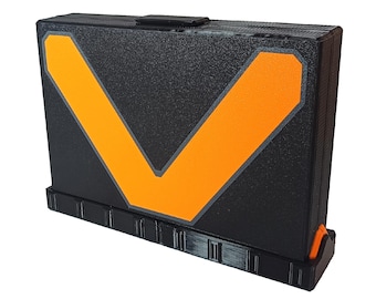 May include: A black folding storage box with an orange V-shaped design on the front. The box has a textured surface and a small handle on the top.