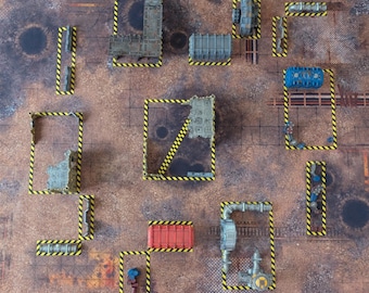 May include: A tabletop gaming mat featuring a weathered, rust-colored industrial terrain surface with various scattered miniature structures, pipes, and containers outlined by yellow and black hazard-striped markings across the grid layout.