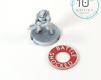 May include: A white painted miniature figure of a soldier holding a gun, standing on a white base. A red plastic token with the words "BATTLE SHOCKED" in white lettering.