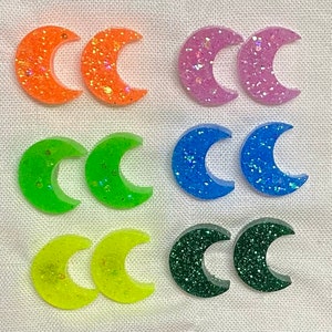 May include: Six pairs of crescent moon shaped earrings in various colors, including orange, green, purple, blue, yellow, and green. Each earring has a glittery finish.