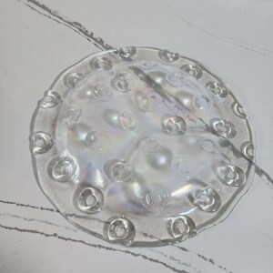 May include: A clear glass plate with a scalloped edge and a raised pattern of small circles. The plate has an iridescent finish.