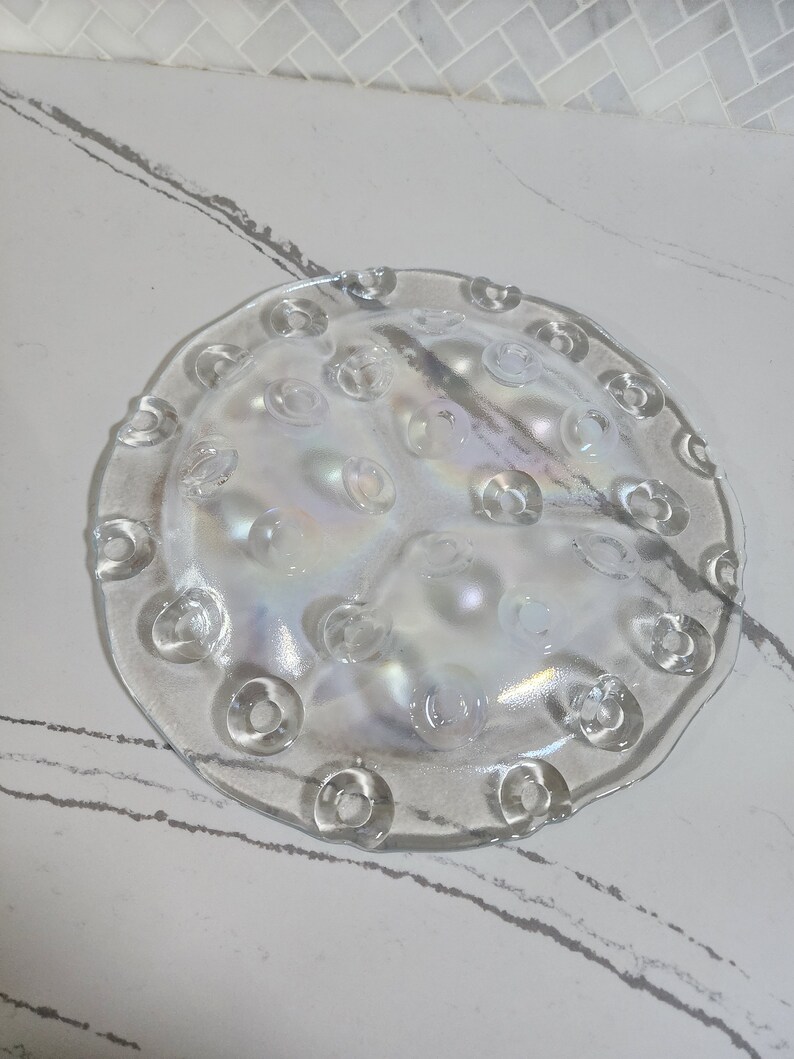 May include: A clear glass plate with a scalloped edge and a raised pattern of small circles. The plate has an iridescent finish.