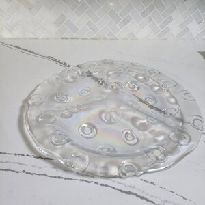 May include: A clear glass serving dish with three sections and a raised rim. The dish has a textured surface with small circles around the edge.