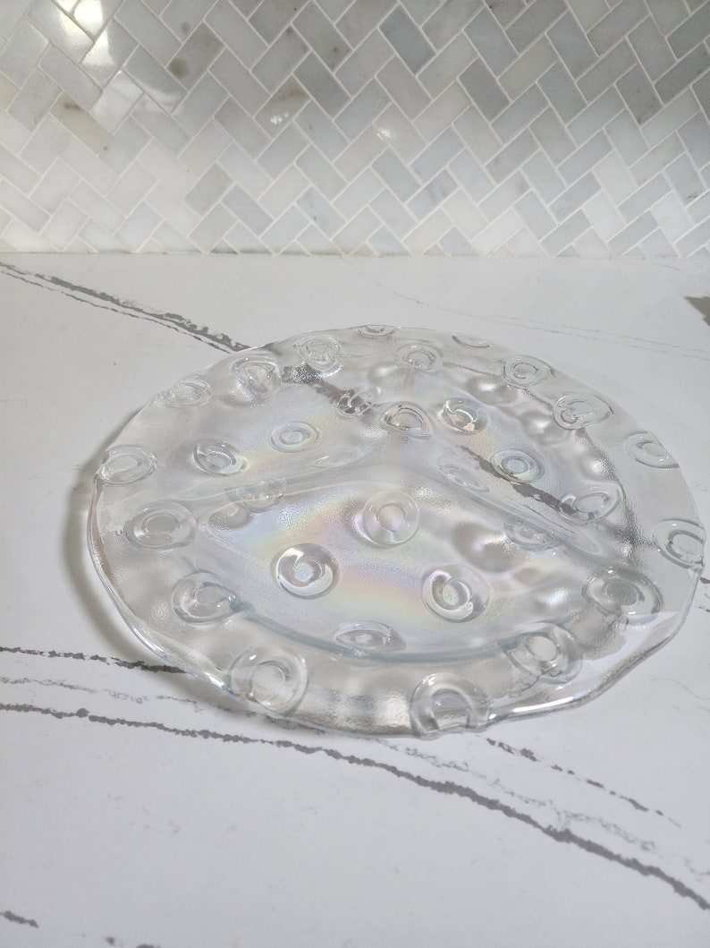 May include: A clear glass serving dish with three sections and a raised rim. The dish has a textured surface with small circles around the edge.