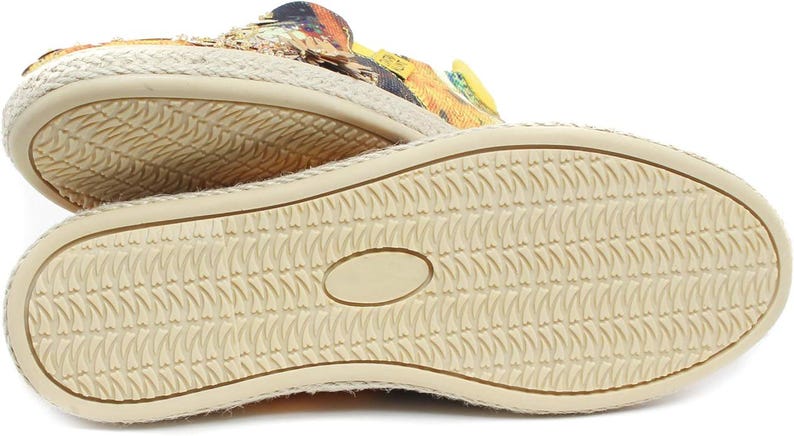 May include: Close-up of the soles of two espadrille shoes. The soles are beige with a textured pattern. The upper part of the shoes features a colorful floral design with yellow, orange, and black accents.