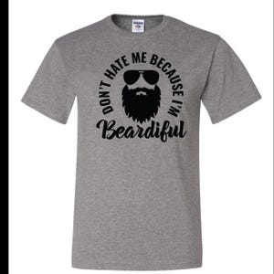 Puede incluir: Camiseta gris con un gráfico negro de un hombre con barba y gafas de sol. El texto dice "Don't hate me because I'm Beardifull."