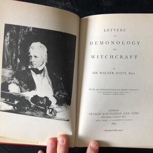 Op de afbeelding: Een open boek met de titel "Letters on Demonology and Witchcraft" van Sir Walter Scott, Bart. De linkerpagina toont een zwart-wit portret. De titel en auteur zijn gedrukt in zwarte inkt.