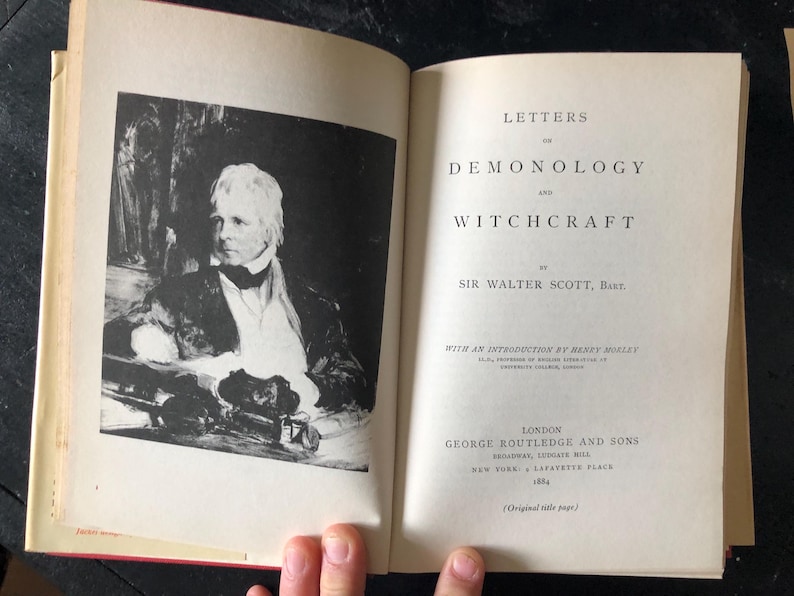 Op de afbeelding: Een open boek met de titel "Letters on Demonology and Witchcraft" van Sir Walter Scott, Bart. De linkerpagina toont een zwart-wit portret. De titel en auteur zijn gedrukt in zwarte inkt.