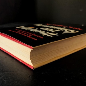 Op de afbeelding: Een hardcover boek getiteld "Demonology and Witchcraft" met een zwarte kaft en rode rand. De titel van het boek staat in witte en rode letters. De pagina's van het boek zijn vergeeld.