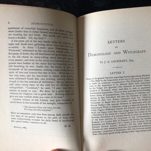 Op de afbeelding: Open boek met de titel "Letters on Demonology and Witchcraft" van J.G. Lockhart. De pagina's zijn vergeeld, wat duidt op ouderdom, met tekst in een klassiek schreeflettertype. Het boek is waarschijnlijk antiek, met focus op historische teksten.