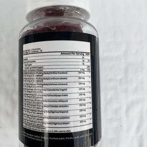 May include: A clear plastic bottle containing red gummies. The bottle has a white lid and a black label detailing nutritional information, such as calories, carbohydrates, and mushroom extracts. The label also states the serving size and number of servings.
