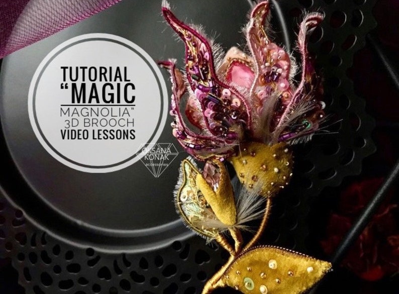 K&ouml;nnte beinhalten: Ein Tutorial f&uuml;r eine 3D-Brosche mit dem Titel "Magnolia Magic" mit Video-Lektionen. Die Brosche ist eine rosa und violette Blume mit goldenen Akzenten und wird auf einem schwarzen Teller pr&auml;sentiert.
