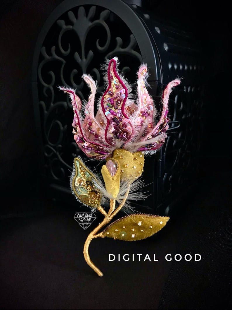 K&ouml;nnte beinhalten: Eine rosa und goldene gestickte Blumenbrosche mit einem zarten Stiel und Bl&auml;ttern. Die Blume ist mit Pailletten und Perlen verziert. Die Brosche ist vor einem schwarzen Hintergrund platziert. "DIGITAL GOOD" steht in wei&szlig;er Schrift unter der Brosche.