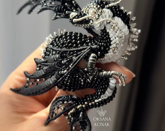 May include: A handcrafted dragon brooch, featuring a detailed design with black beads, white sequins, and silver accents. The dragon's wings are made of black lace. The brooch is a unique piece of jewelry.