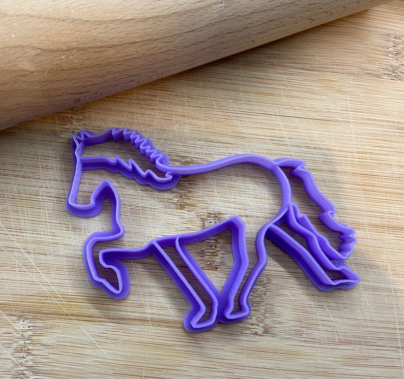 May include: Purple plastic horse cookie cutter on a wooden surface.
