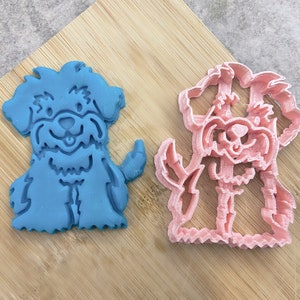 May include: Two dog-shaped cookie cutters, one blue and one pink, on a wooden surface.