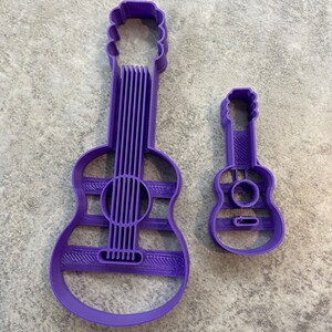 Puede incluir: Dos cortadores de galletas de guitarra de pl&aacute;stico morado. El cortador m&aacute;s grande es una forma de guitarra est&aacute;ndar, mientras que el cortador m&aacute;s peque&ntilde;o es una forma de ukelele.