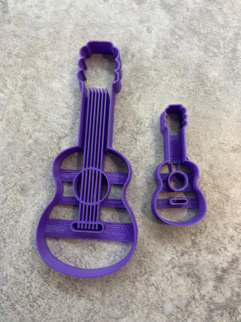 Puede incluir: Dos cortadores de galletas de guitarra de pl&aacute;stico morado. El cortador m&aacute;s grande es una forma de guitarra est&aacute;ndar, mientras que el cortador m&aacute;s peque&ntilde;o es una forma de ukelele.