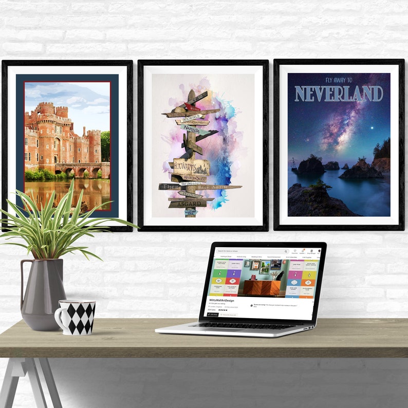 May include: Three framed prints on a white brick wall above a wooden desk with a laptop, a vase with a green plant, and a mug. The prints are of a castle, a watercolour painting of a signpost with various destinations, and a poster with the text "Fly Away To Neverland".