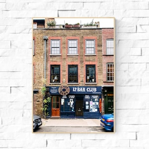 Puede incluir: Un edificio de ladrillo con una puerta azul y un letrero que dice "12 Bar Club". El edificio tiene un aspecto vintage y está ubicado en una calle con otros edificios.