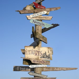 May include: A wooden signpost with multiple directional arrows pointing to different fictional locations, including Hogwarts, Narnia, Asgard, and Neverland. The signpost is against a blue sky.