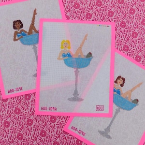 May include: Needlepoint canvases featuring women in blue cocktail glasses. Each canvas has a pink border and a unique woman design. The canvases are on a pink floral background. The text "ADD-109A", "ADD-109B", and "ADD-109C" are visible.