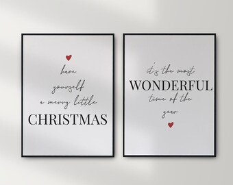 May include: Two framed prints with white backgrounds and black frames hanging on a white wall above a bed with white bedding. The print on the left says "treat yourself to a merry little CHRISTMAS" with a red heart. The print on the right says "it's the most WONDERFUL time of the year" with a red heart.