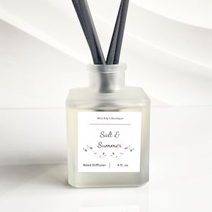 May include: A frosted glass reed diffuser with dark gray reeds. The label reads "Salt & Summer" with floral accents and "Reed Diffuser | 4 fl. oz." The product is from Miss Kay's Boutique.