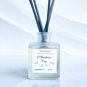 May include: A frosted glass reed diffuser with dark gray reeds. The label reads "O' Christmas Tree" with a floral design. The bottle contains 4 fl oz of liquid. The product is from Miss Kay's Boutique.
