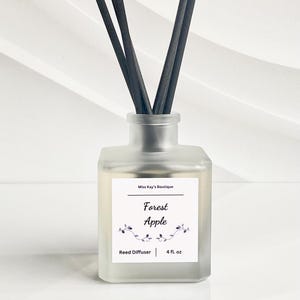 May include: A frosted glass reed diffuser with black reeds. The label reads "Forest Apple" and "4 fl. oz." The product is from "Miss Kay's Boutique". The background is white.
