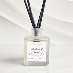 Peut inclure: Un diffuseur de roseaux en verre dépoli avec des roseaux noirs. L'étiquette indique "Wonderland Forest" avec des motifs floraux. La bouteille contient 118 ml de parfum et provient de Miss Kay's Boutique.