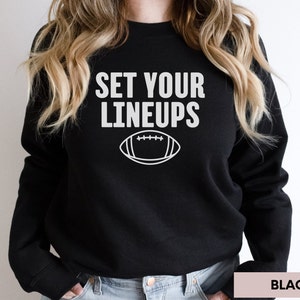 May include: Black sweatshirt with white text that reads "Set Your Lineups" and a white outline of a football.