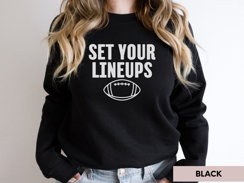 May include: Black sweatshirt with white text that reads "Set Your Lineups" and a white outline of a football.