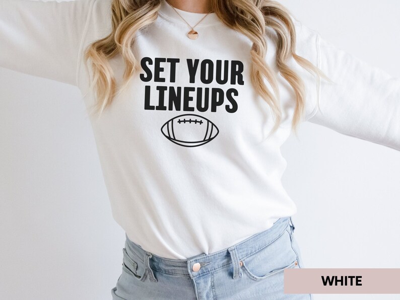 May include: White sweatshirt with black text that says "SET YOUR LINEUPS" and a black outline of a football.